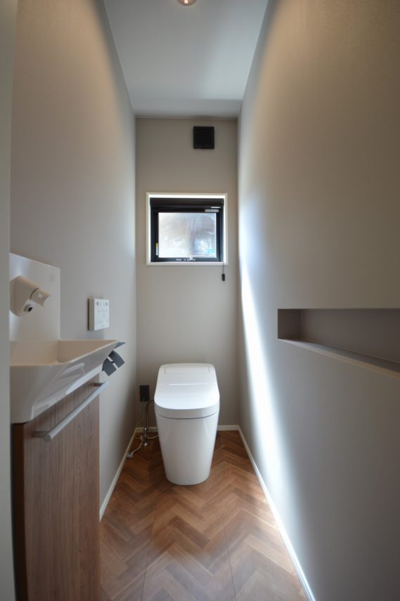 【トイレ】</br> グレーの壁紙で落ち着きのある空間。ヘリンボーンの床がアクセントになります。</br> ニッチはトイレットペーパーがちょうど入る大きさに。それ自体がデザインにもなります。