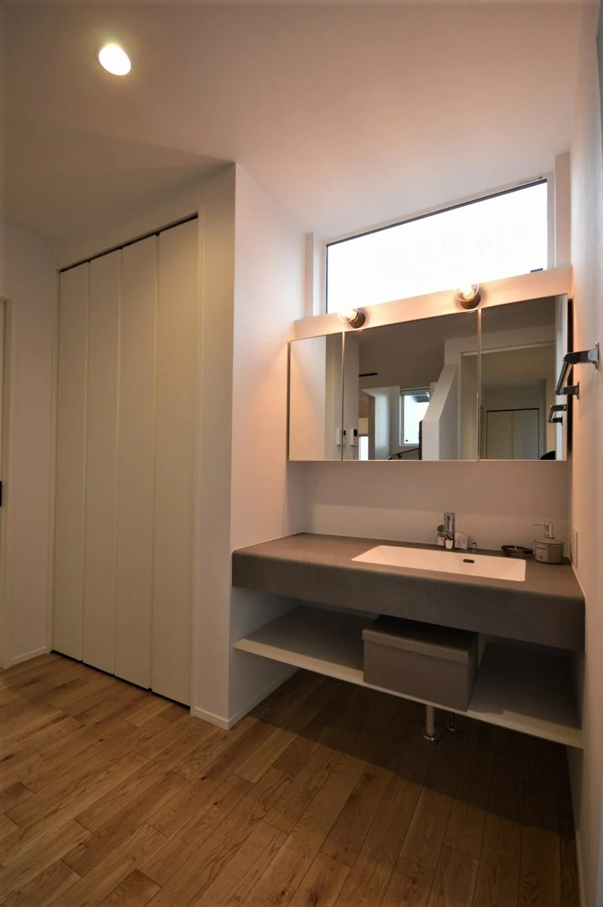 W1200の幅広洗面台。モルタル調で人気の仕様に。 収納は大容量のミラーキャビネットとし、照明器具をこだわることで全体的に造作の雰囲気に。 玄関からも接続でき、LDKの一部の空間なので、常に冷暖房の効いた空間で、快適に使用できます。