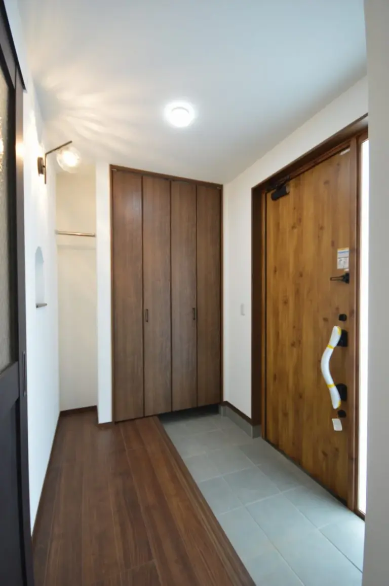 照明器具の光がデザインになる玄関。大容量の壁面収納と、必要なだけのコート掛けを設置。