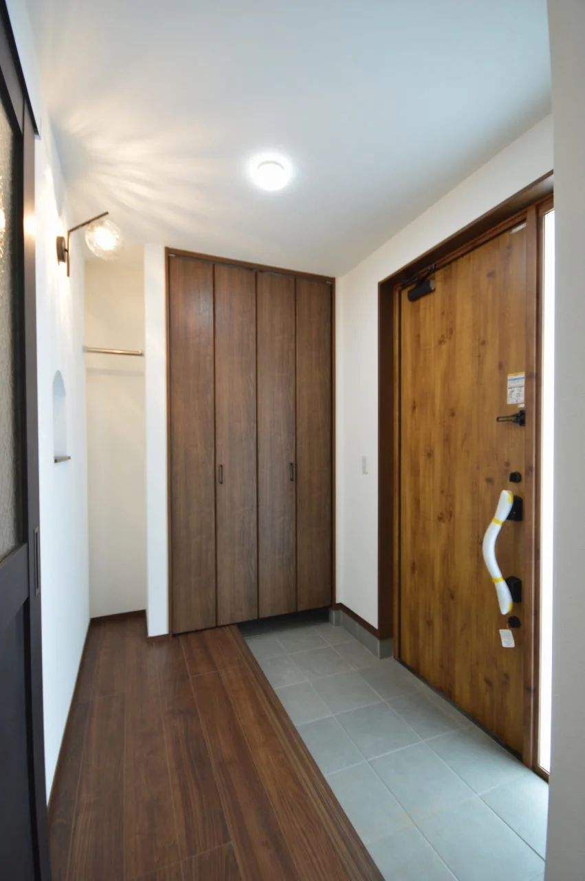 照明器具の光がデザインになる玄関。大容量の壁面収納と、必要なだけのコート掛けを設置。