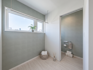 淡いグリーンの壁紙と物干しバーを配した、トイレと自然に繋がる明るいサニタリー